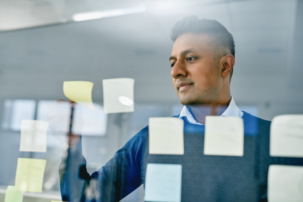 Man working on clear glass with post-it notes for article on project manager career path
