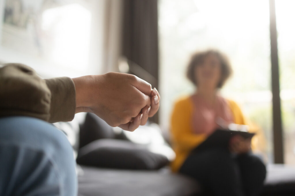 Close-up photo of a teenage girl's hands with fingers crossed nervously. She is in a therapy session with her psychotherapist.