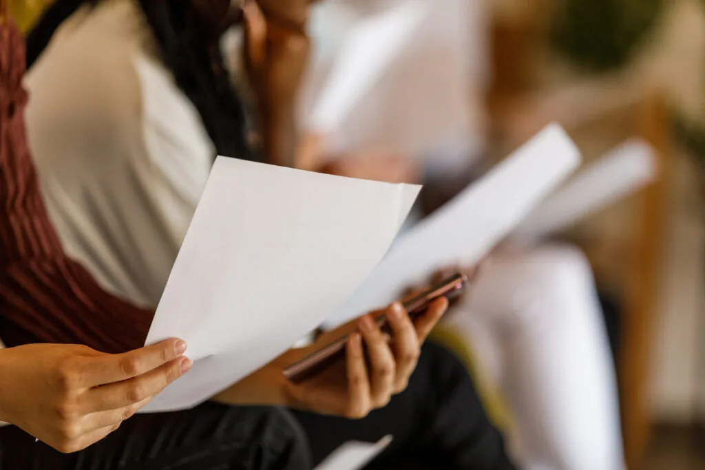 Selective focus shot of diverse group of business people sitting in line against the wall, chatting, preparing and reading their resumes and cover letters when waiting for a job interview meeting.