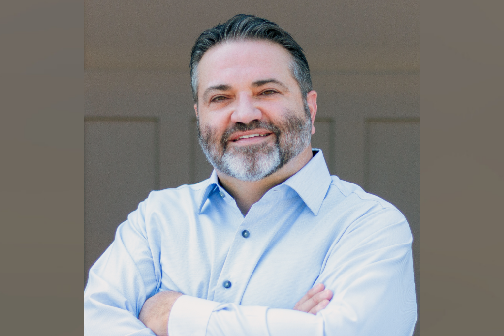 Online MSIDBT alumnus Joseph Sherbanee poses in blue button-up with arms crossed smiling.