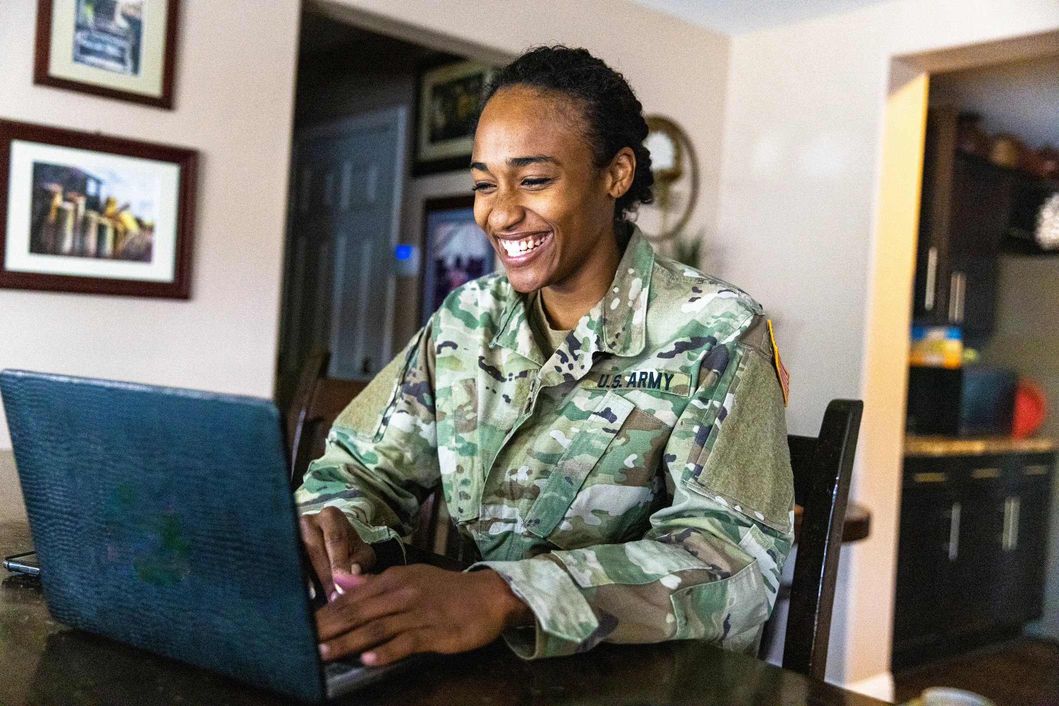 Read about: A young Army service member sits at home, smiling at her laptop as she takes an online class.