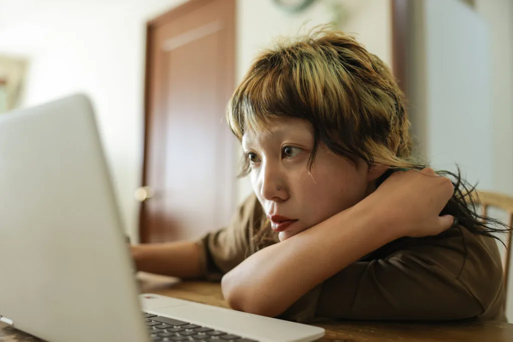 Young woman with colorful hair looks at laptop screen.