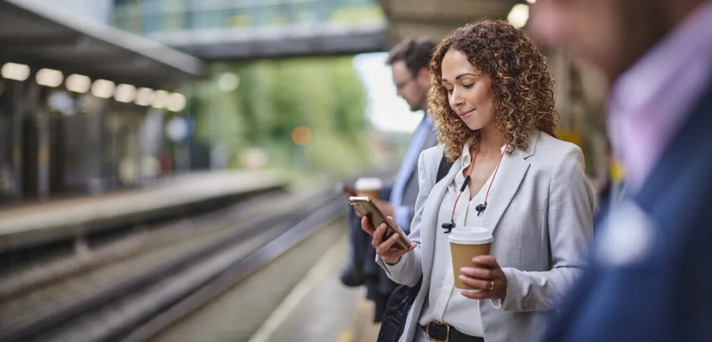 A woman checks her phone while waiting for the metro to come. If you're worried you're getting ghosted by an employer, here's what to do.