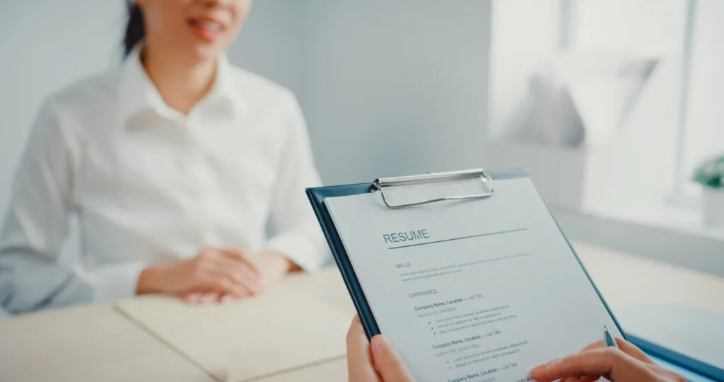 A woman in a white button up shirt sits across the table from someone reading her resume. Find out how to write a functional resume in this article.
