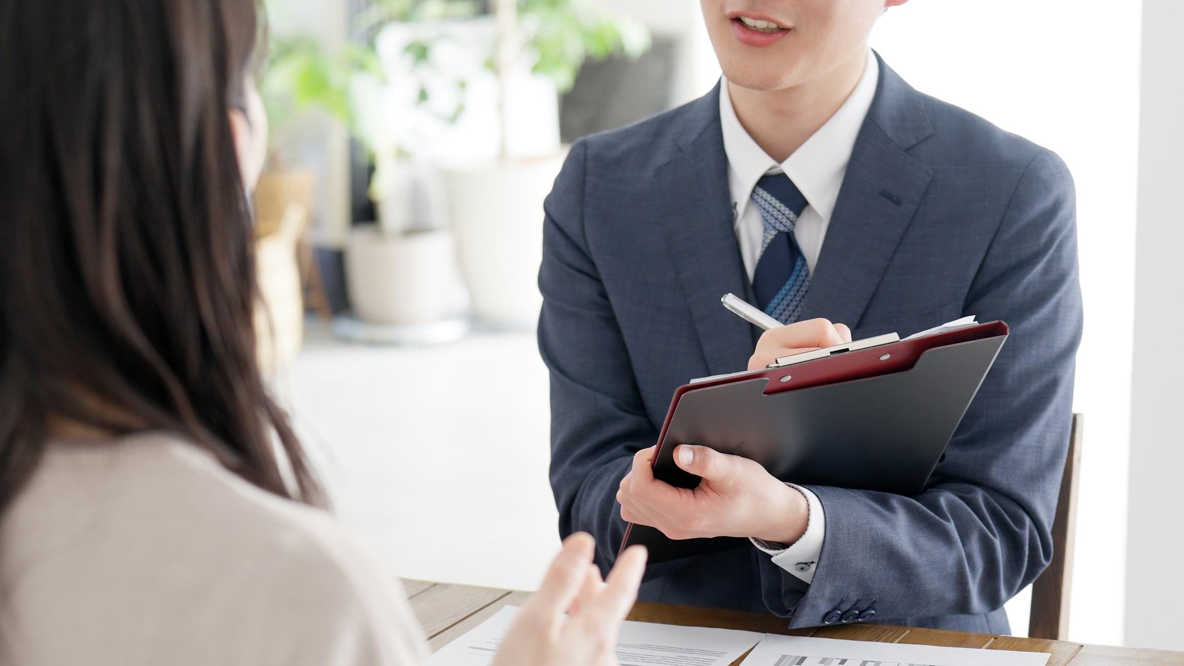 Read about: A man in a suit holding a clipboard speaks to a woman with her back to the camera. Here is a guide to answering the most-asked interview questions.