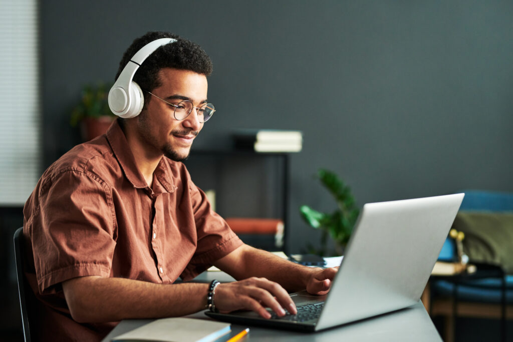 A young, smiling man wearing white headphones types on a laptop keyboard. Learn more about the best jobs for introverts.
