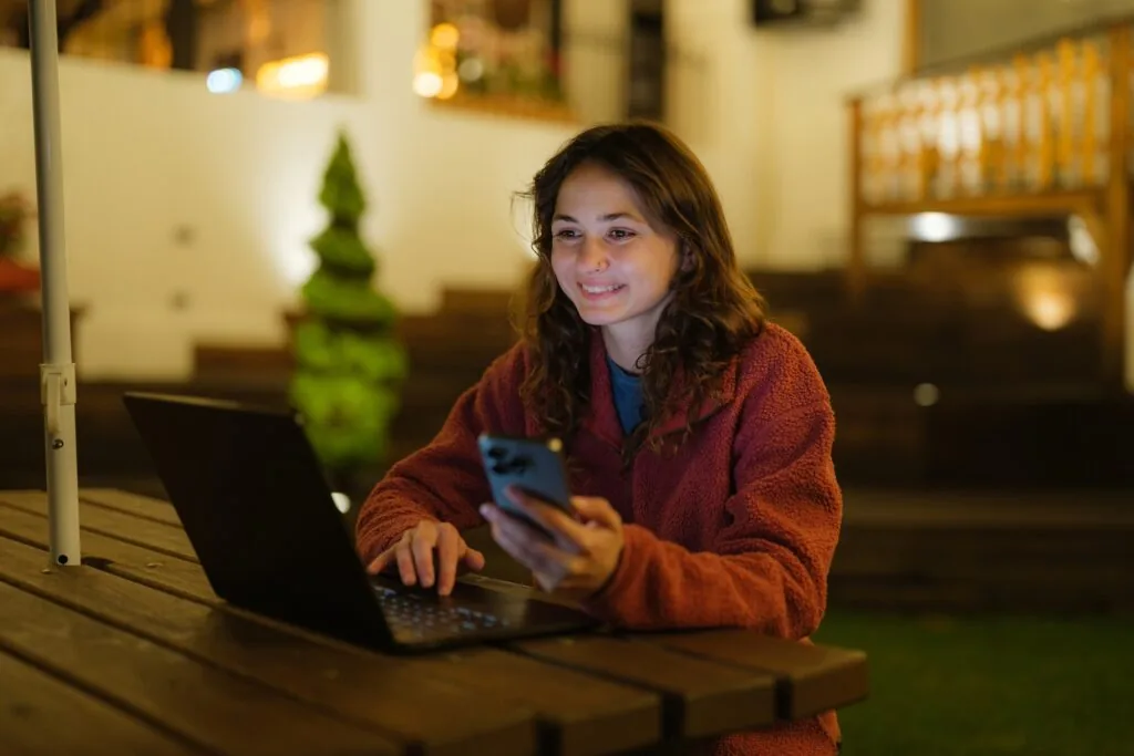 Woman Using Smartphone And Laptop Working On The Backyard At Night